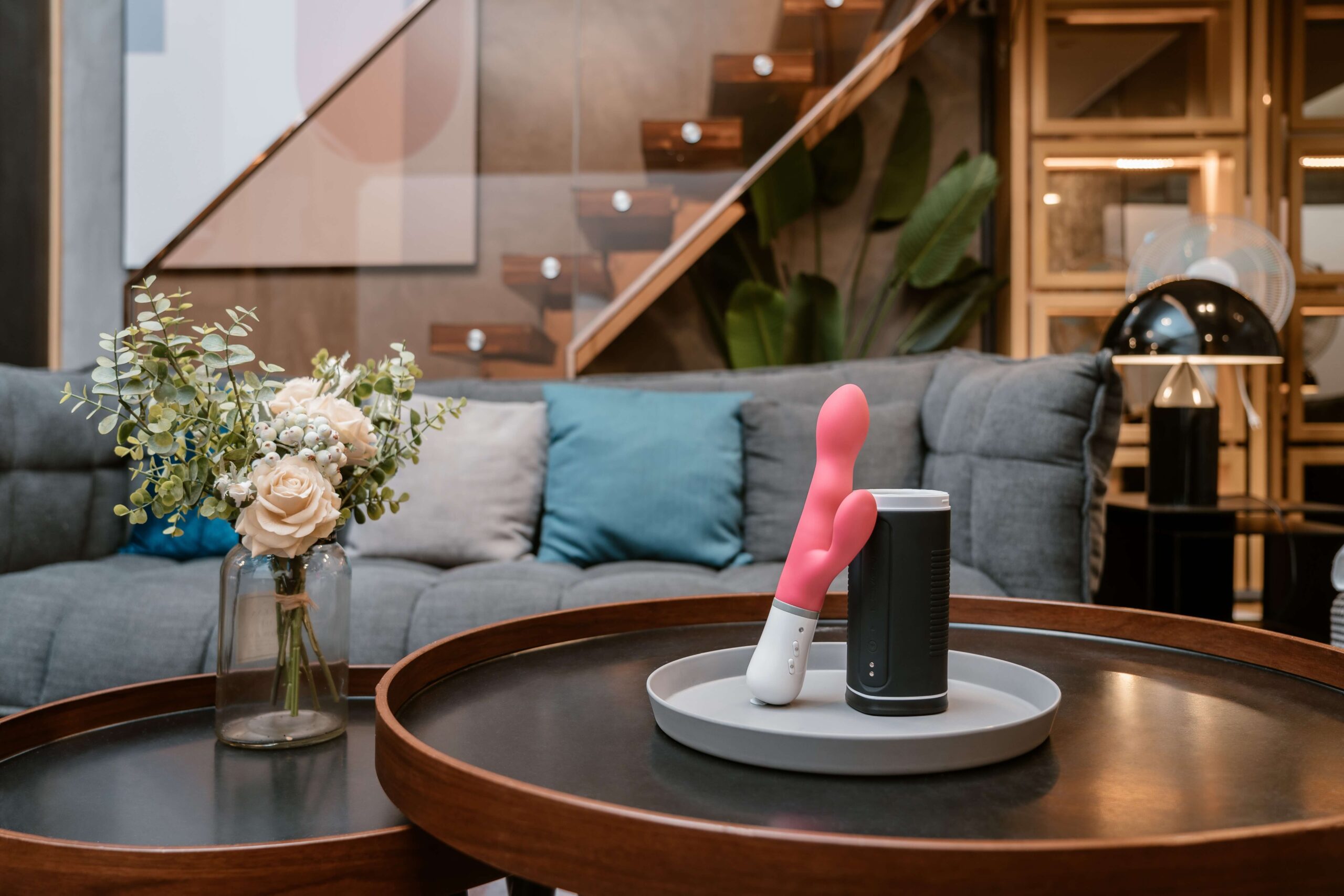 A living room with a vibrator, bluetooth speaker, and vase with roses on the coffee table